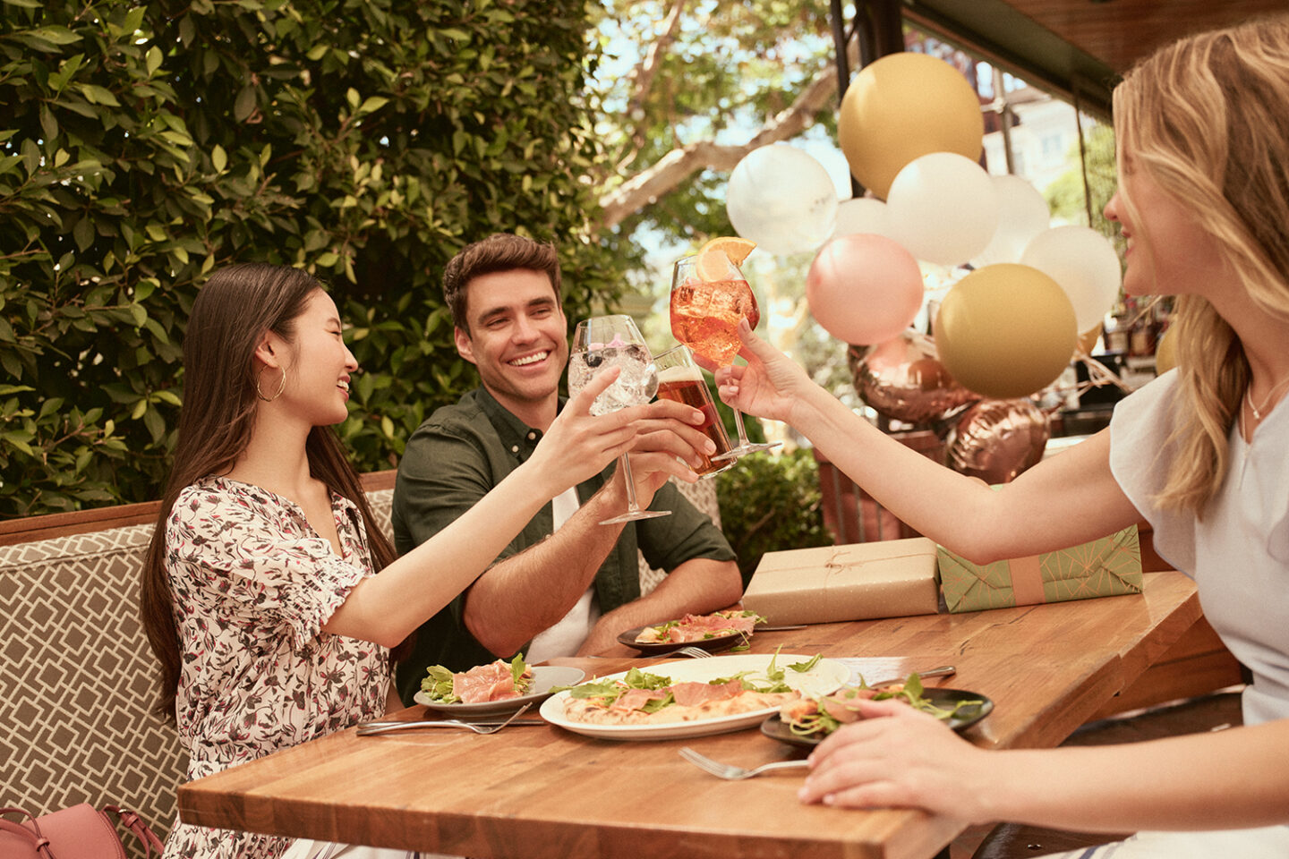 Group of friends celebrating at a Restaurant, drinking wine, wrapped gifts, balloons, food on the table