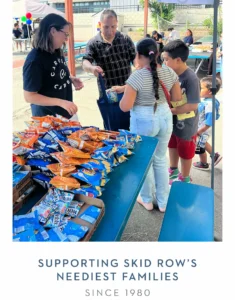 Man gives snacks to a young girl at an outdoor donation event, with chips and fruit snacks on the table.